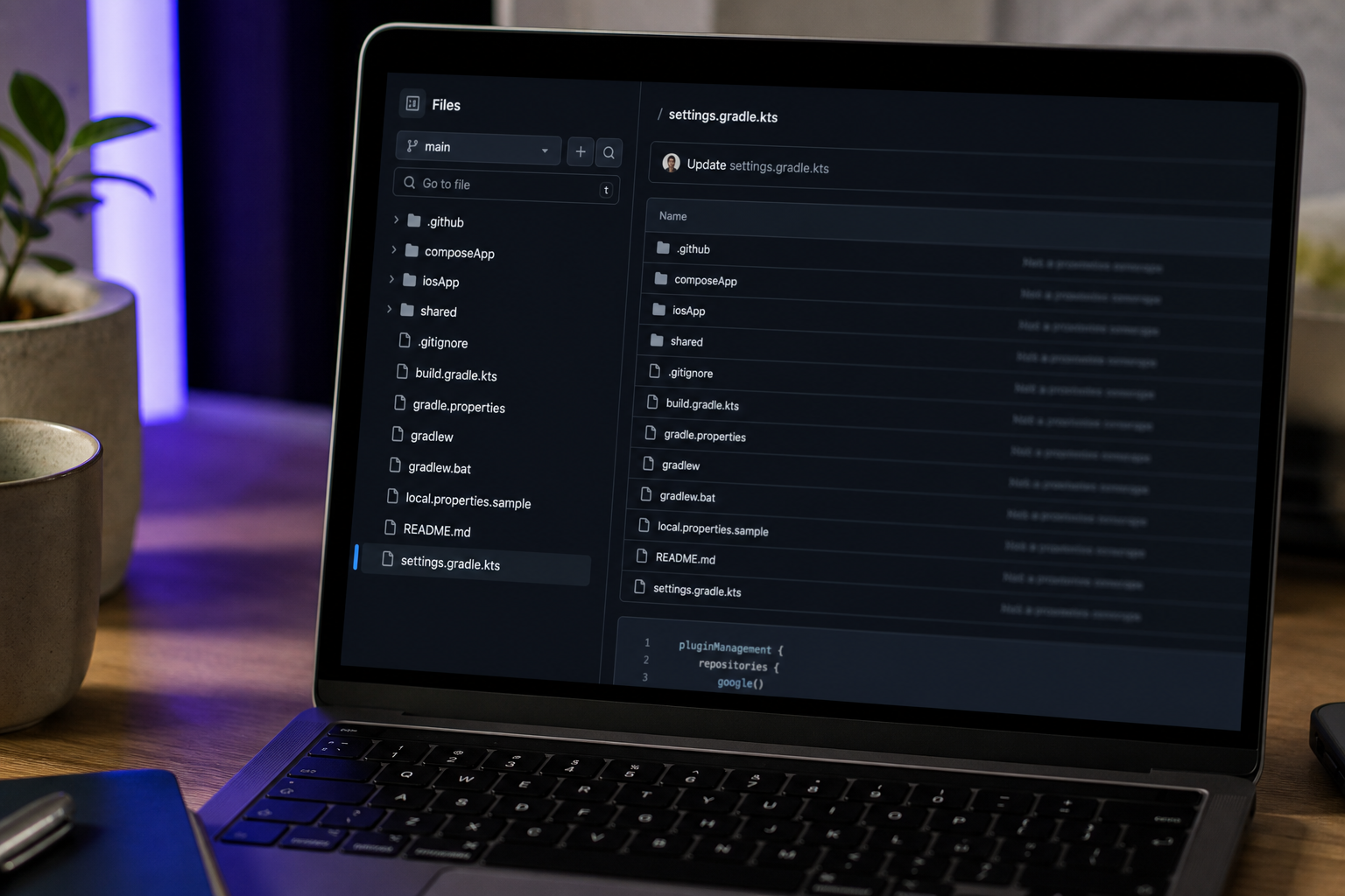 Close-up of a laptop screen showing a GitHub repository page — specifically the file tree of a Kotlin Multiplatform project (visible: composeApp/, iosApp/, shared/, settings.gradle.kts). Slight depth-of-field blur on the surrounding desk. Authentic,