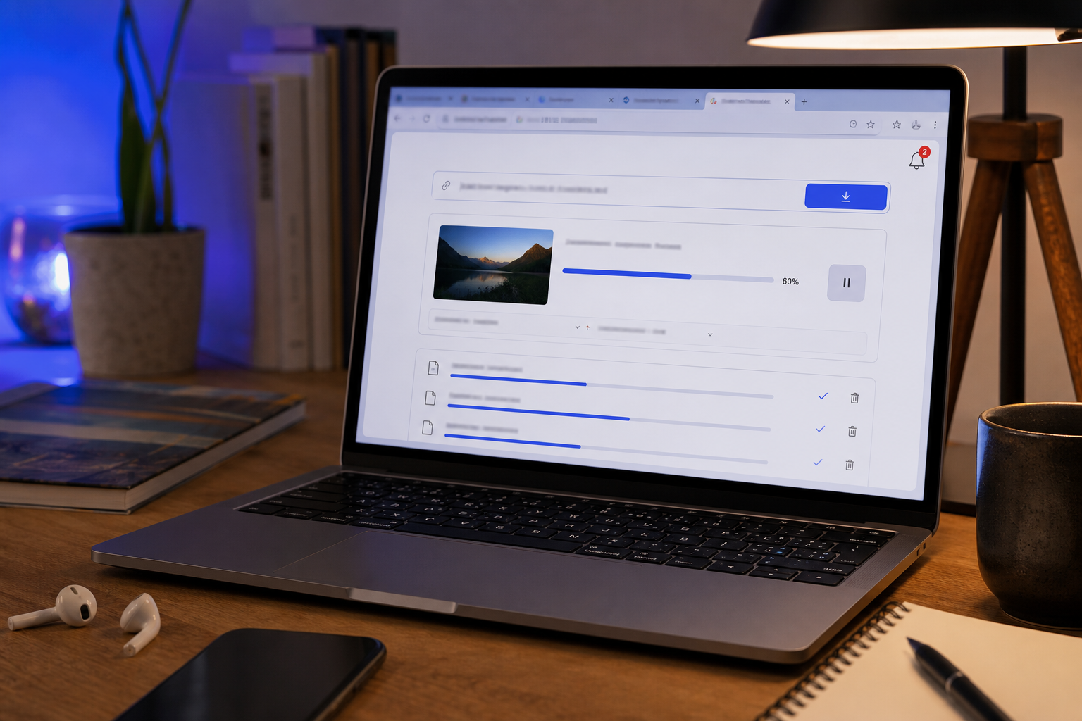 A laptop screen at an angle showing a generic video downloader interface mid-use, with multiple browser tabs open and a small notification badge visible. Warm desk lighting, slightly cluttered workspace — conveys real user, real workflow, not stock-p