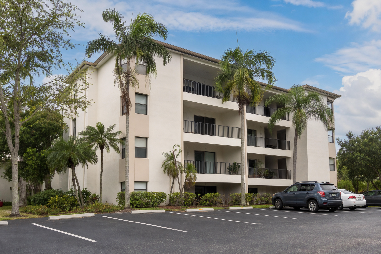 Exterior daytime shot of a clean, mid-rise multi-family building (6–12 units, three stories). South Florida palette — pastels or white stucco. Visible balconies and a parking lot. Should look like an asset a serious investor would underwrite, not a l