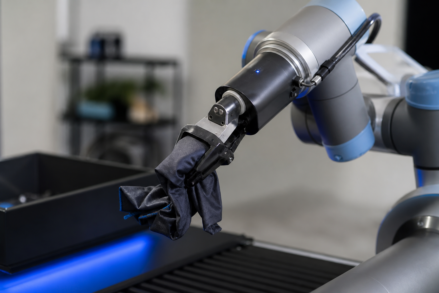 Close-up of a Franka Panda or Universal Robots UR5e gripper holding an irregular crumpled fabric or novel-shape part against a clean lab background, shallow depth of field, side angle, showing a deployed manipulator executing a learned grasping polic