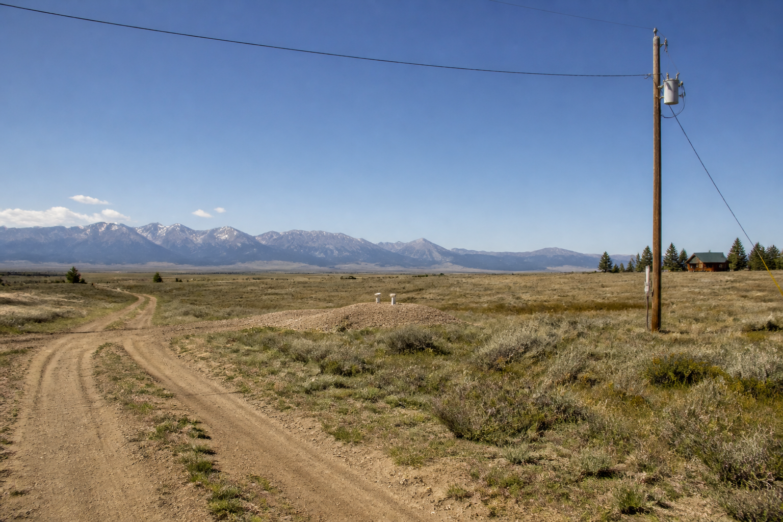 Rural Colorado parcel showing visible infrastructure realities — a single power pole with a long span of line crossing open ground toward a property, a dirt private road, and a septic mound discernible in the middle distance.